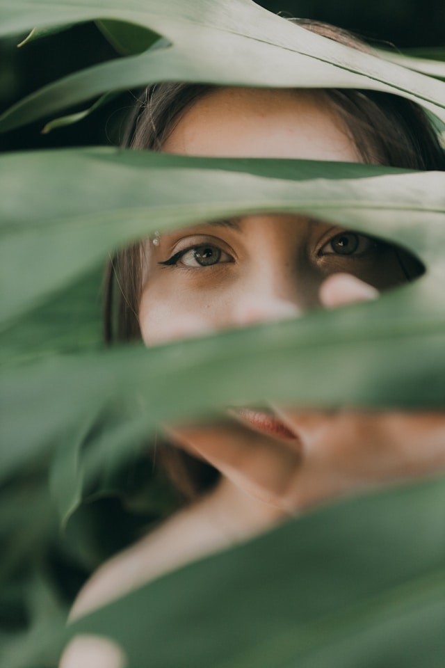 young woman hiding behind large plant leaf
