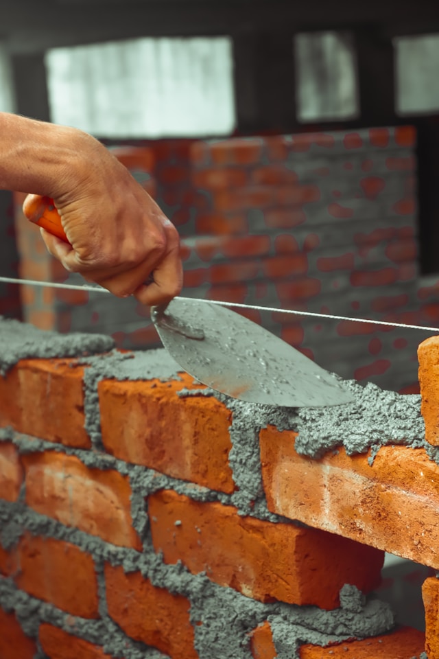 An image of two hands building a brick wall together, but one hand is carefully placing a brick while the other is holding a level. It illustrates "Love builds up" and the careful "leveling" of our freedom.